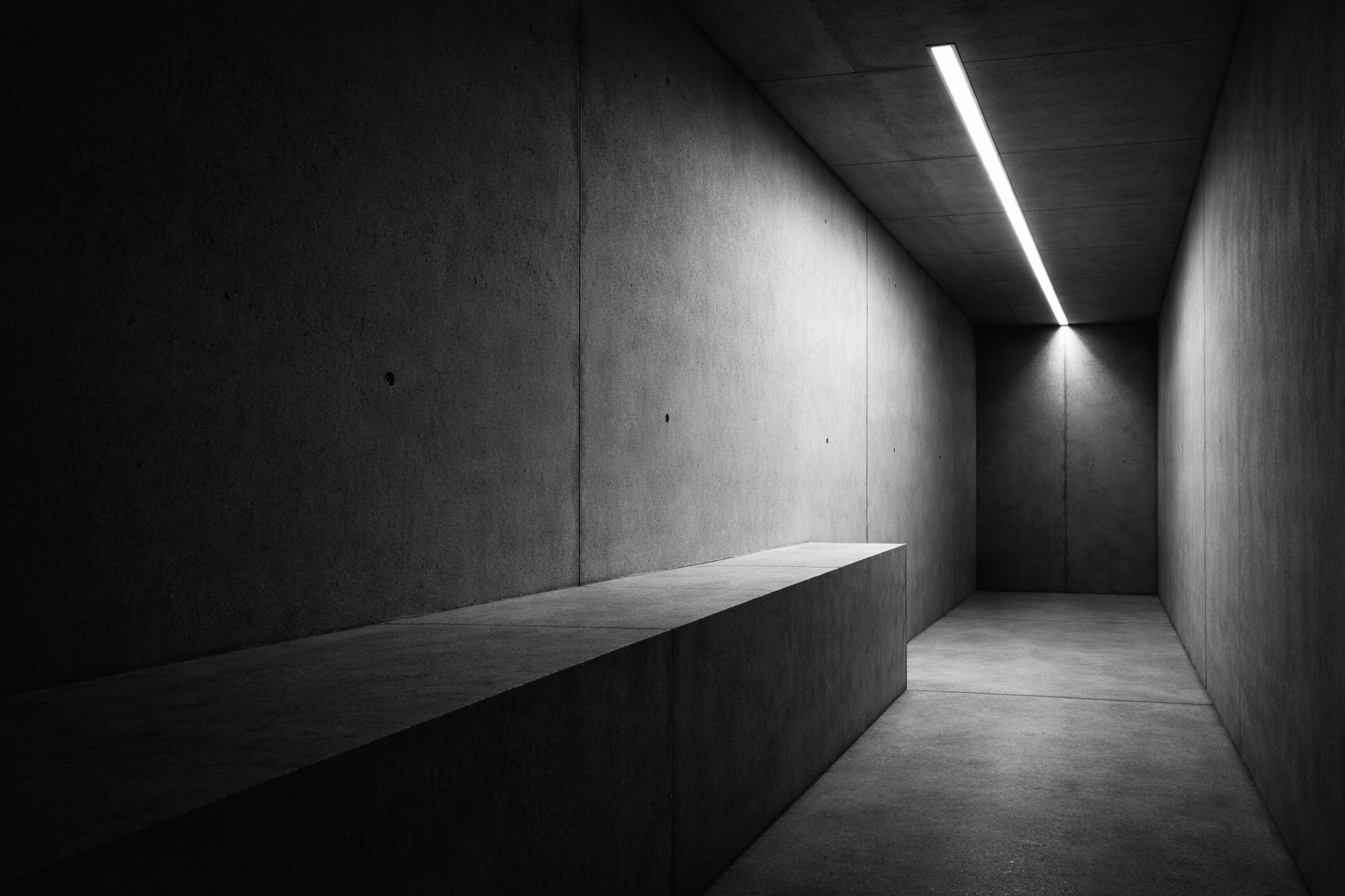 High-contrast monochrome corridor with concrete surfaces and a narrow line of overhead light.